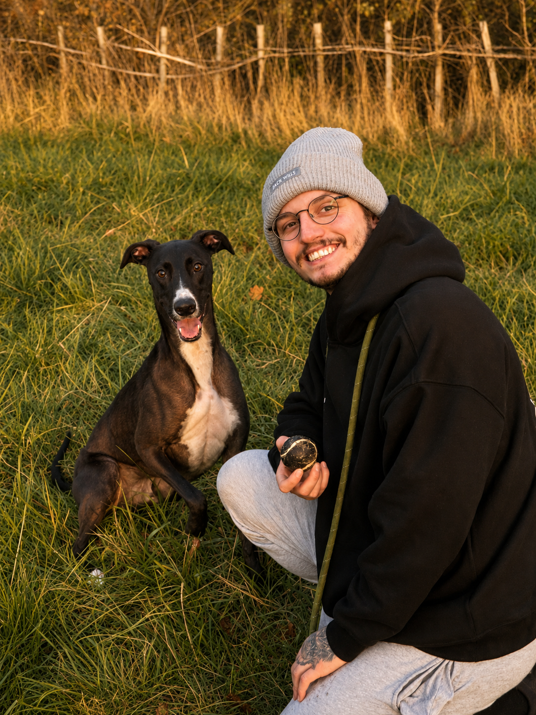 Harry Morgan crouching next to a happy black and white dog in a grassy field